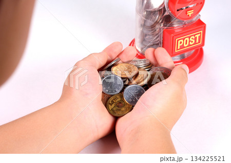 小銭を持つ子どもの手とポスト型の貯金箱 小銭を持つ子どもの手とポスト型の貯金箱 134225521