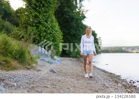 Woman walking on a scenic trail by the lake in outdoor activewear Woman walking on a scenic trail by the lake in outdoor activewear 134226388