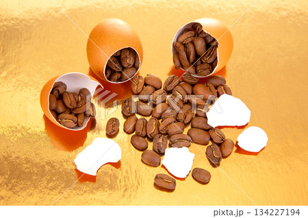 egg reveals coffee beans inside, scattered on a reflective golden surface with broken eggshells egg reveals coffee beans inside, scattered on a reflective golden surface with broken eggshells 134227194
