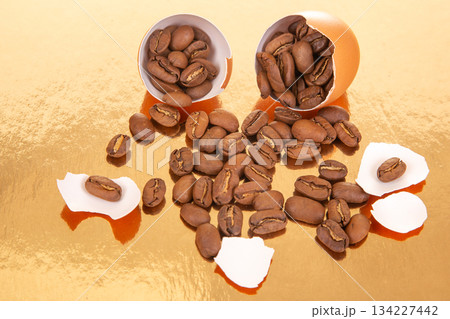 split egg reveals coffee beans inside scattered on a reflective golden surface with broken eggshells split egg reveals coffee beans inside scattered on a reflective golden surface with broken eggshells 134227442