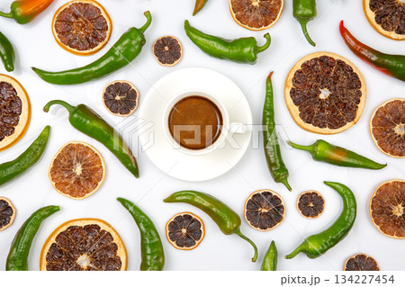 A white cup of cappuccino with foam, surrounded by dried orange slices and green chili peppers A white cup of cappuccino with foam, surrounded by dried orange slices and green chili peppers 134227454
