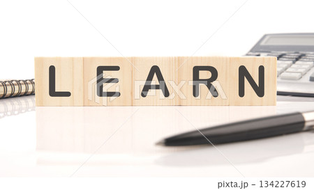 Wooden blocks spelling LEARN rest on a white surface near a pen, notebook, and calculator, suggesting educational pursuits and growth 134227619