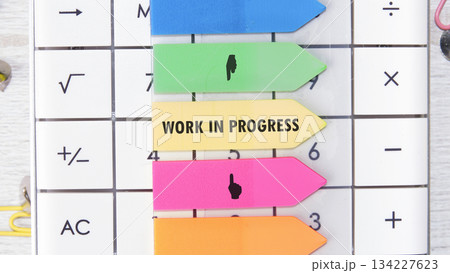 A calculator features colorful sticky notes, including one boldly displaying Work In Progress, alongside mathematical symbols. This close-up captures a focused, process-oriented scene A calculator features colorful sticky notes, including one boldly displaying Work In Progress, alongside mathematical symbols. This close-up captures a focused, process-oriented scene 134227623