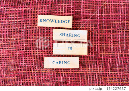 Wooden blocks with words placed on a vibrant red woven fabric highlight the idea that sharing knowledge promotes caring and understanding among people in a thoughtful manner 134227687