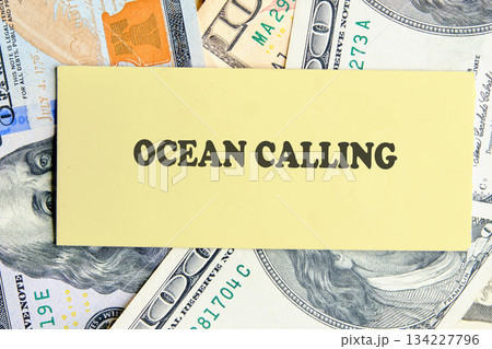 A warm note with the words Ocean Calling rests atop scattered dollar bills, symbolizing a desire for adventure and the journey to coastal destinations filled with beauty 134227796