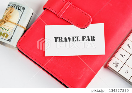 A bold travel card rests atop a bright red wallet, next to a stack of cash and a simple calculator, inviting dreams of faraway places and exciting experiences waiting to unfold 134227859