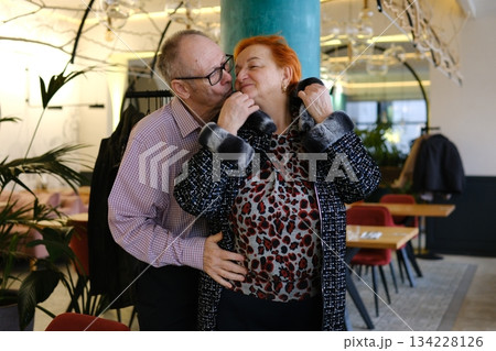 A man helps a woman put on her jacket and kisses her on the cheek. An adult couple, love, family, relationship, in a restaurant. 134228126