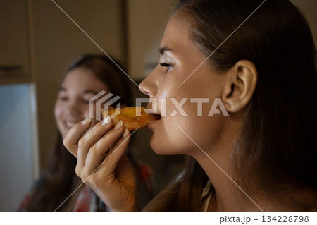 Woman Daughter Pastry Kitchen: Nighttime snacking mother and daughter enjoy a late-night pastry in their kitchen. Woman Daughter Pastry Kitchen: Nighttime snacking mother and daughter enjoy a late-night pastry in their kitchen. 134228798