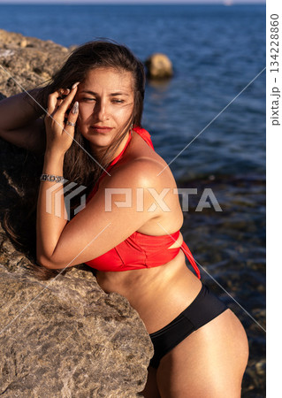 Woman bikini sea, young woman in red and black swimwear leaning on a rock by the ocean during summer vacation Woman bikini sea, young woman in red and black swimwear leaning on a rock by the ocean during summer vacation 134228860