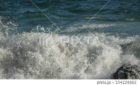 Ocean Waves Crashing. Powerful ocean waves collide with a shore rock, generating white foam and spray on a sunny day. Ocean Waves Crashing. Powerful ocean waves collide with a shore rock, generating white foam and spray on a sunny day. 134228862
