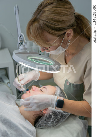 Cosmetology Dermatologist Facial Treatment: Clinic procedure, expert performs skincare treatment, patient receives professional care. 134229000