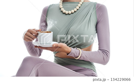 Woman holds a steaming cup in a modern setting with a focus on fashion and lifestyle 134229066
