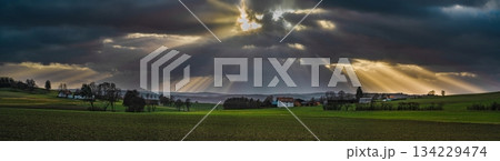 the sun's rays pierce the clouds over the agricultural field 134229474