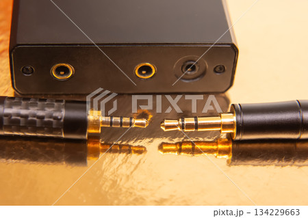 Close-up of two 3.5mm audio jacks with gold connectors on a reflective golden surface Close-up of two 3.5mm audio jacks with gold connectors on a reflective golden surface 134229663