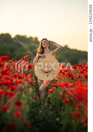Woman in Poppy Field Holding Straw Hat 134229688