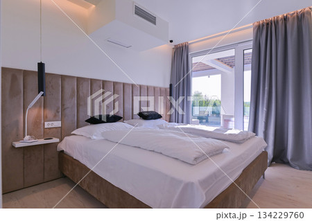 Bright, modern bedroom featuring a comfortable bed, sleek desk, and a large sliding glass door opening to a private balcony with stunning green landscape views, perfect for relaxation and serene 134229760
