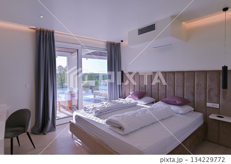Bright, modern bedroom featuring a comfortable bed, sleek desk, and a large sliding glass door opening to a private balcony with stunning green landscape views, perfect for relaxation and serene 134229772