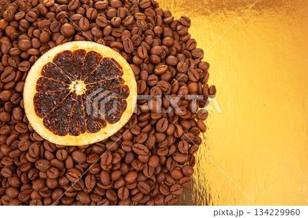 Vibrant dried orange slices contrast with dark coffee beans on a golden reflective surface Vibrant dried orange slices contrast with dark coffee beans on a golden reflective surface 134229960