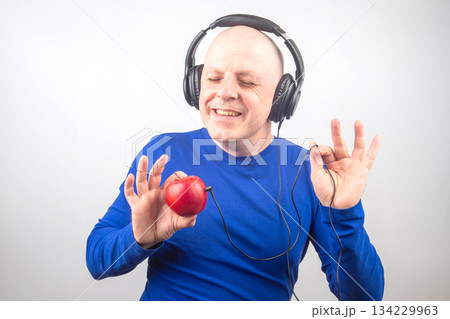 bald man with headphones listens to music through a red apple player bald man with headphones listens to music through a red apple player 134229963