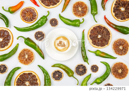 Cappuccino in a white cup centered among dried orange slices and green chili peppers 134229971