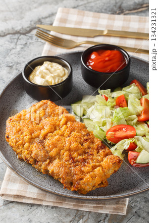 Tender Sicilian beef steak in a Parmesan and breadcrumb crust served with a fresh salad and two sauces close-up on a plate. Vertical 134231321