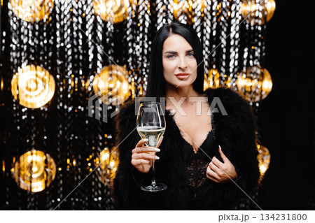 Young happy woman in trendy evening fur coat looking at camera and smiling with glass of champagne 134231800