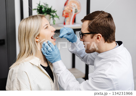 Doctor using inspection spatula to examine patient throat. ENT doctor doing throat exam of a woman. Patient opened her mouth to throat check-up 134231966