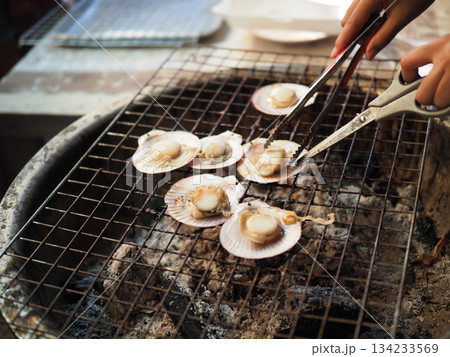 Grilled scallop seafood shell barbeque charcoal street food tongs outdoor cooking with savory aroma and warmth 134233569
