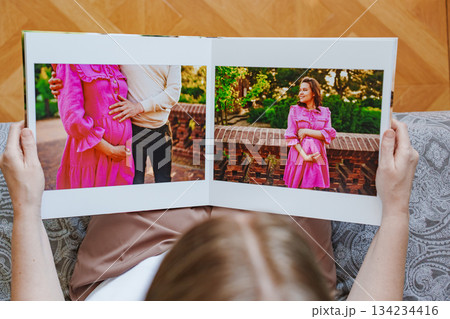 woman is holding and flipping through a photo book with a pregnancy photo shoot 134234416