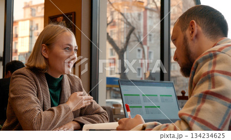 Two young people working together on a laptop in a cozy cafe setting 134234625