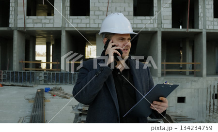 Male engineer talking on the phone outside a modern construction building Male engineer talking on the phone outside a modern construction building 134234759