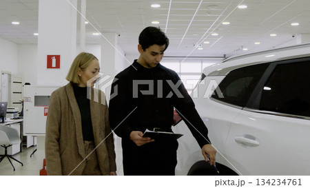 Car salesman showing a young couple the exterior of a new white car 134234761
