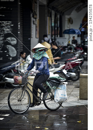 Woman wearing a blue shirt and a blue hat rides a bicycle 134235078