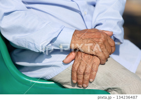 Senior person resting hands on knees while seated outdoors in a sunny park setting during the afternoon 134236487