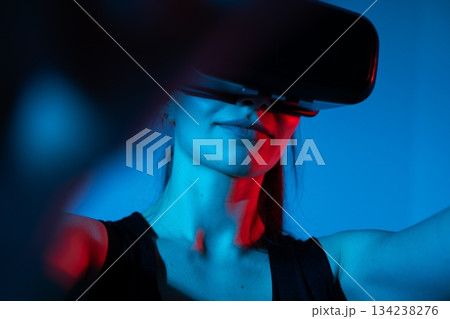Female user interacting with virtual reality headset in vivid blue and red futuristic lighting space Female user interacting with virtual reality headset in vivid blue and red futuristic lighting space 134238276