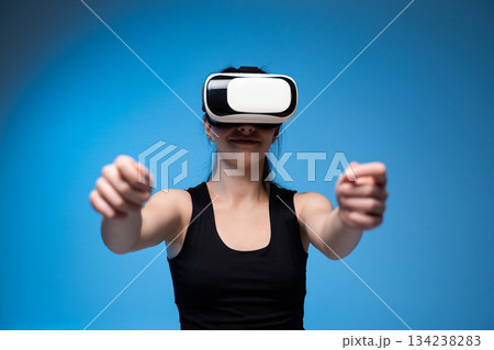 Smiling woman using VR headset with extended arms interacting in immersive digital blue environment Smiling woman using VR headset with extended arms interacting in immersive digital blue environment 134238283