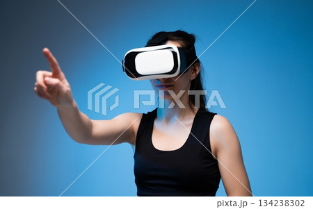 Woman interacting with virtual reality technology while pointing toward digital elements in VR space Woman interacting with virtual reality technology while pointing toward digital elements in VR space 134238302