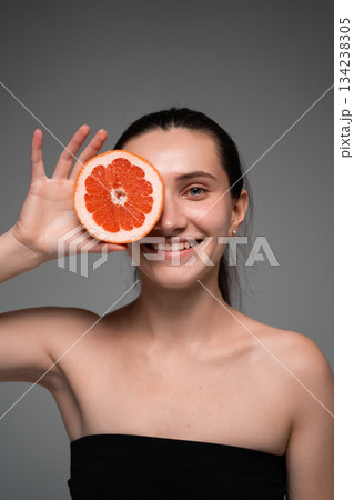 Smiling woman holding grapefruit slice to face, promoting citrus skincare, natural freshness and healthy beauty Smiling woman holding grapefruit slice to face, promoting citrus skincare, natural freshness and healthy beauty 134238305