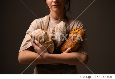 A female baker holds three rustic handmade bread loaves with varied crust textures 134238306
