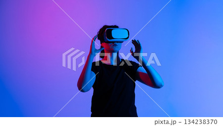 Woman adjusting VR headset while preparing for virtual experience under vibrant blue and pink neon lights Woman adjusting VR headset while preparing for virtual experience under vibrant blue and pink neon lights 134238370