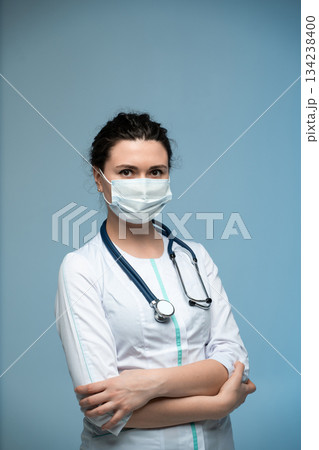Female medical professional in mask and white uniform with stethoscope posing on blue background 134238400