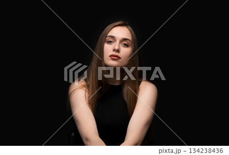 Calm studio portrait of a young woman with neutral facial expression against a dark background Calm studio portrait of a young woman with neutral facial expression against a dark background 134238436