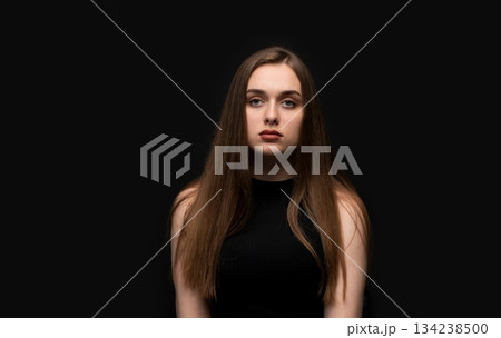 Young woman posing for neutral studio portrait on black background with natural expression and straight posture Young woman posing for neutral studio portrait on black background with natural expression and straight posture 134238500