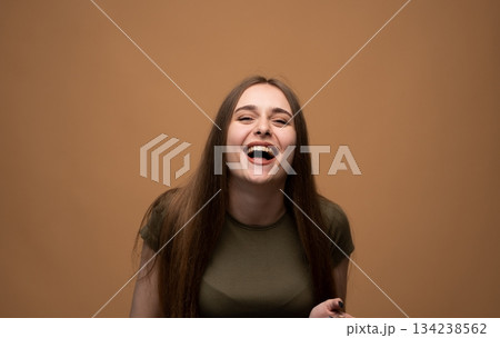 Laughing young woman leaning forward, expressive joyful portrait with positive emotion on warm soft background 134238562