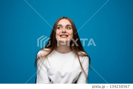 Happy young woman looking up with smiling expression, joyful emotional portrait on blue studio backdrop Happy young woman looking up with smiling expression, joyful emotional portrait on blue studio backdrop 134238567