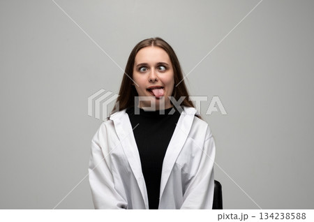Woman making silly face with crossed eyes and tongue out in playful studio portrait expression 134238588