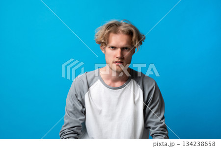 Serious young man staring intensely at camera on blue background, focused and concentrated expression Serious young man staring intensely at camera on blue background, focused and concentrated expression 134238658