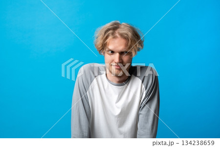 Young man giving sly sideways glance with playful expression on clean bright blue backdrop Young man giving sly sideways glance with playful expression on clean bright blue backdrop 134238659