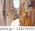 Woman in dress strolls through colorful streets of Spanish coastal town of La Vila Joiosa or Villajoyosa. sunny winter atmosphere highlights charm of Mediterranean architecture and quiet seaside life 134239350
