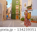 Woman in dress strolls through colorful streets of Spanish coastal town of La Vila Joiosa or Villajoyosa. sunny winter atmosphere highlights charm of Mediterranean architecture and quiet seaside life 134239351